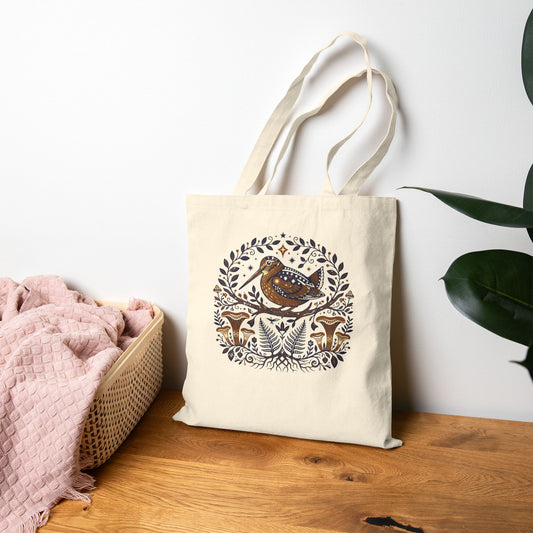 Tote bag with nature-themed design and woodcock on a wooden surface with a white wall background