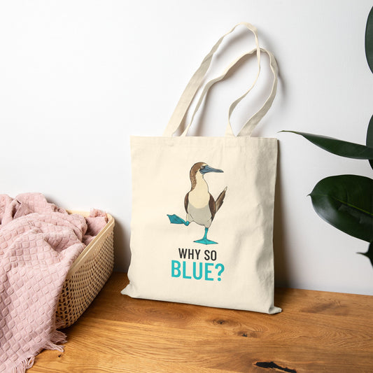 Tote bag with a blue-footed booby bird graphic and 'Why So Blue?' text on a wooden surface.