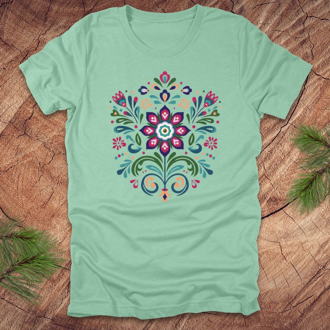 Mint green t-shirt with a colorful dutch inspired floral design on a wood background.