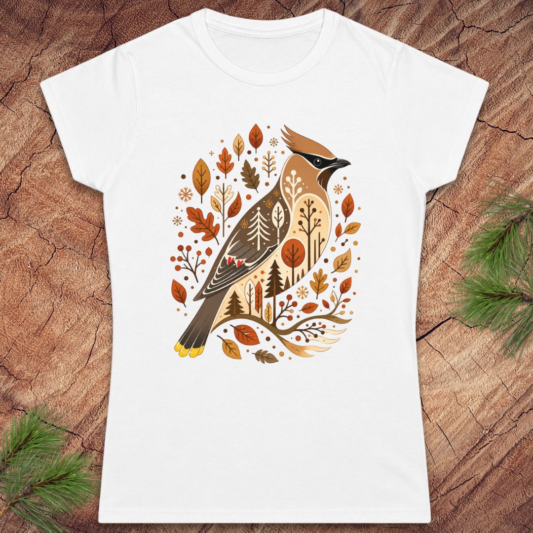 A white short-sleeve crewneck t-shirt featuring a detailed graphic of a cedar waxbird surrounded by autumn leaves and trees, displayed flat on a rustic wood background with pine branches in the corners.