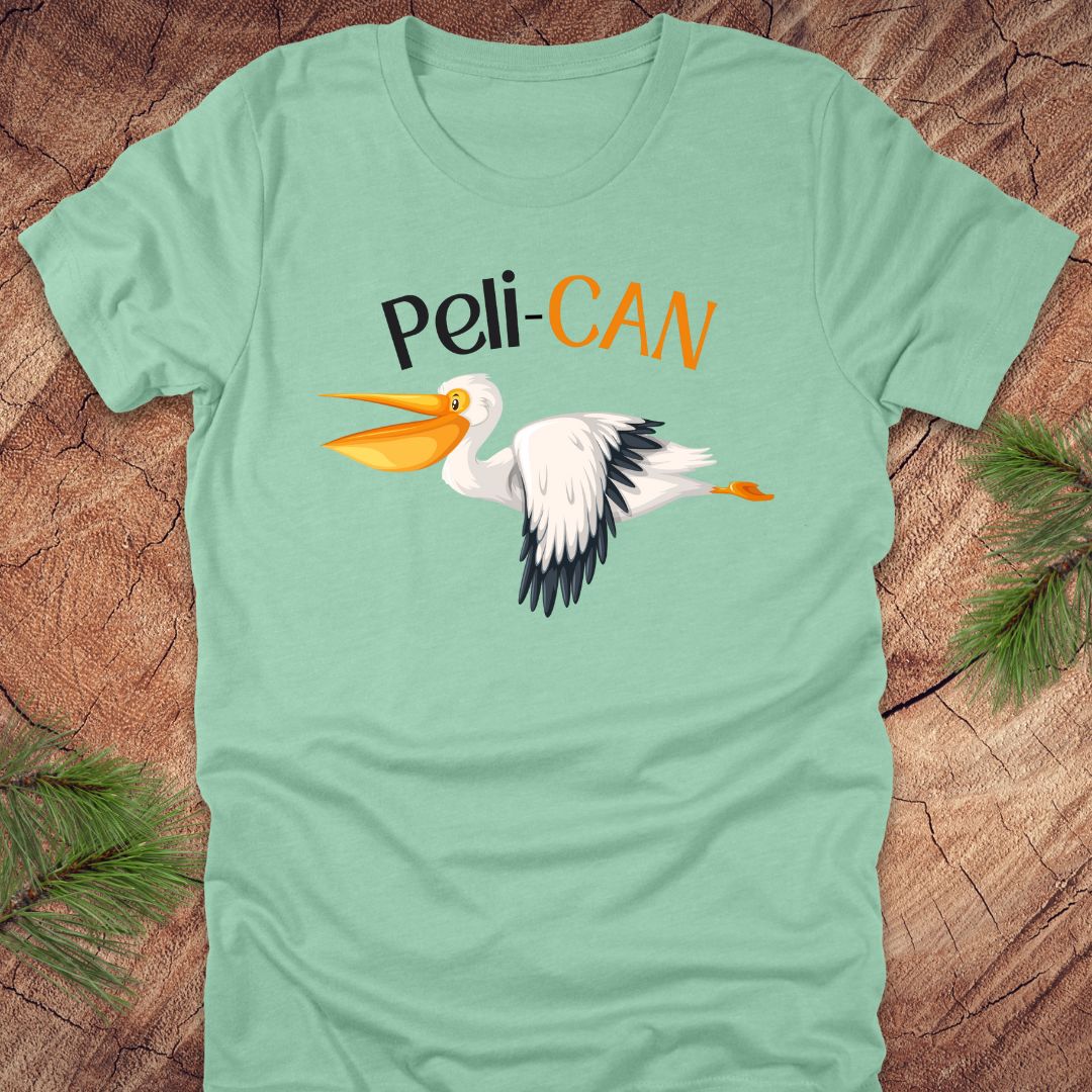 Light green t-shirt with a pelican graphic and 'Peli-CAN' text on a wooden surface.