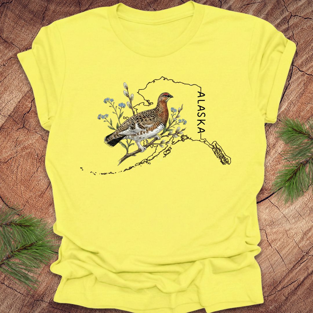 Yellow t-shirt with an Alaska-themed graphic featuring a bird and nature elements on a wooden surface.