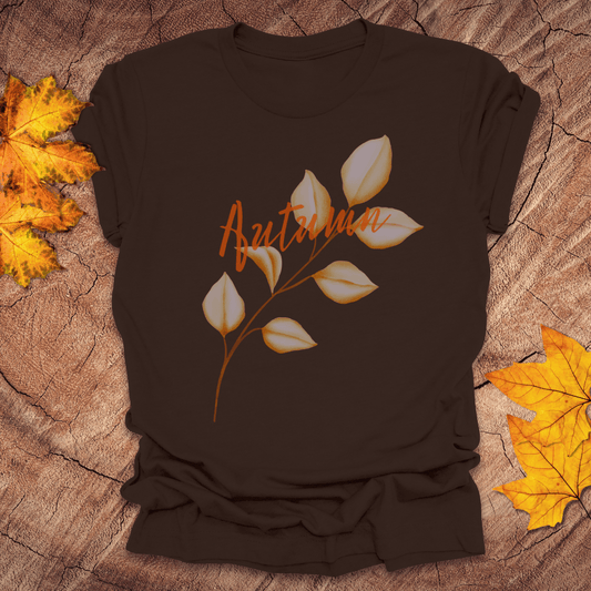 Brown t-shirt with 'Autumn' and leaf design on a wooden surface with fall leaves.