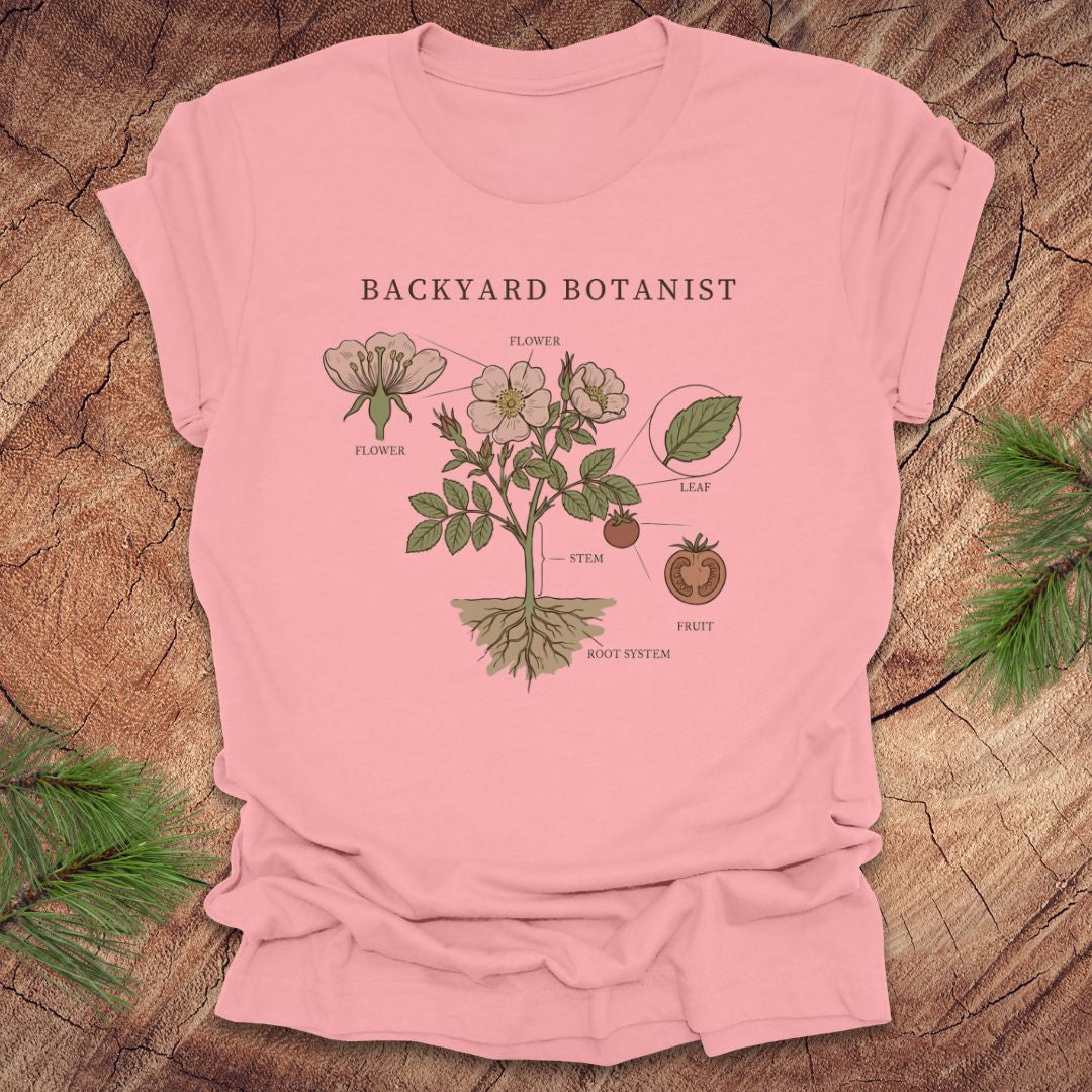 Pink t-shirt with botanical design and 'Backyard Botanist' text on a wooden surface.