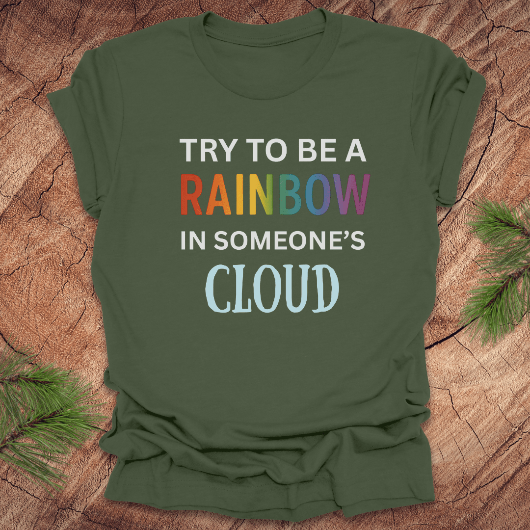 Green t-shirt with colorful text 'Try to be a rainbow in someone's cloud' on a wooden surface