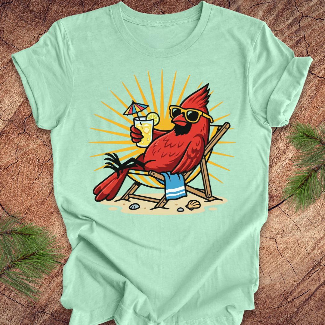 Mint green t-shirt with a red cardinal wearing sunglasses and a hat, holding a drink, on a wooden surface.