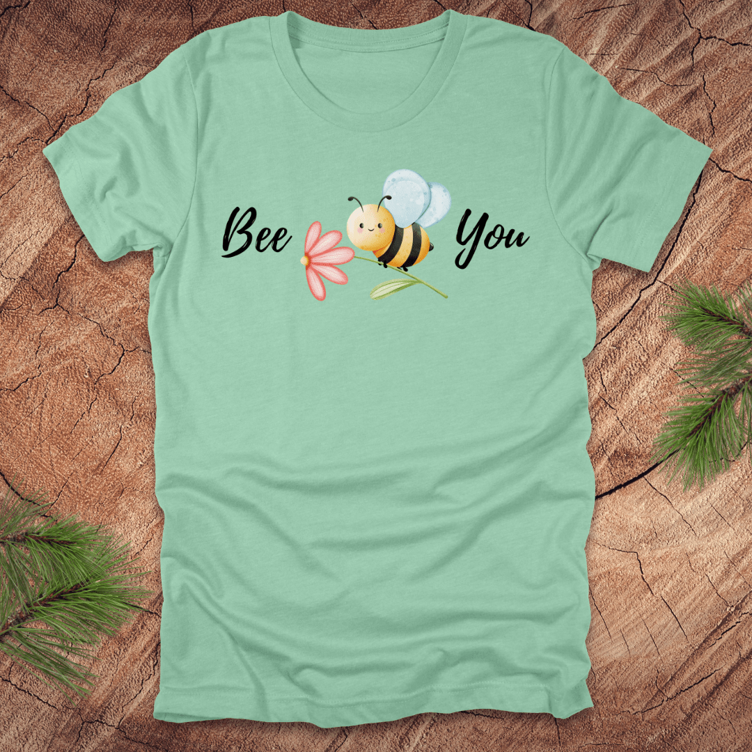 Mint green tshirt with a cute bee and the text, "bee you" on a wooden background.