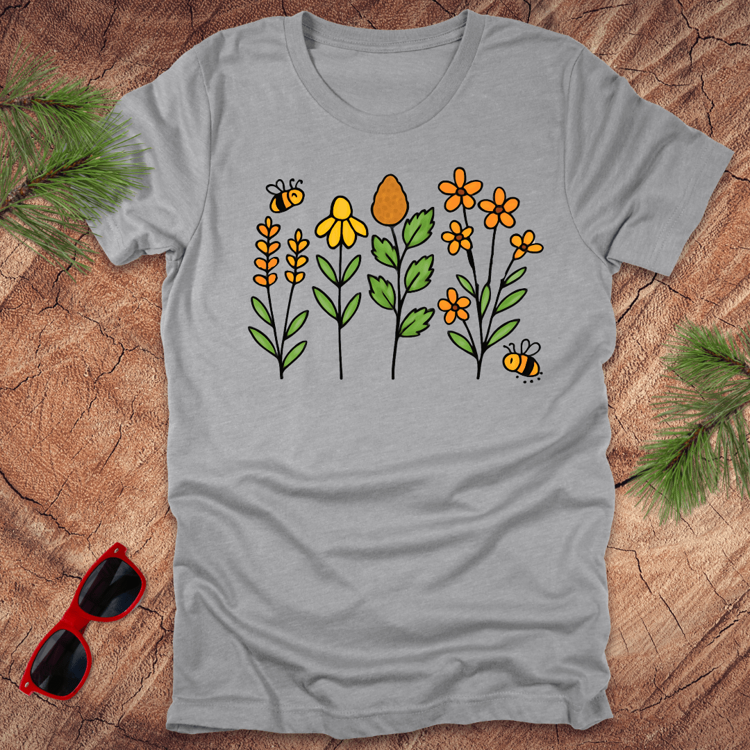 Grey tshirt with a flower and bee graphic in oranges and yellows, on a wood background.