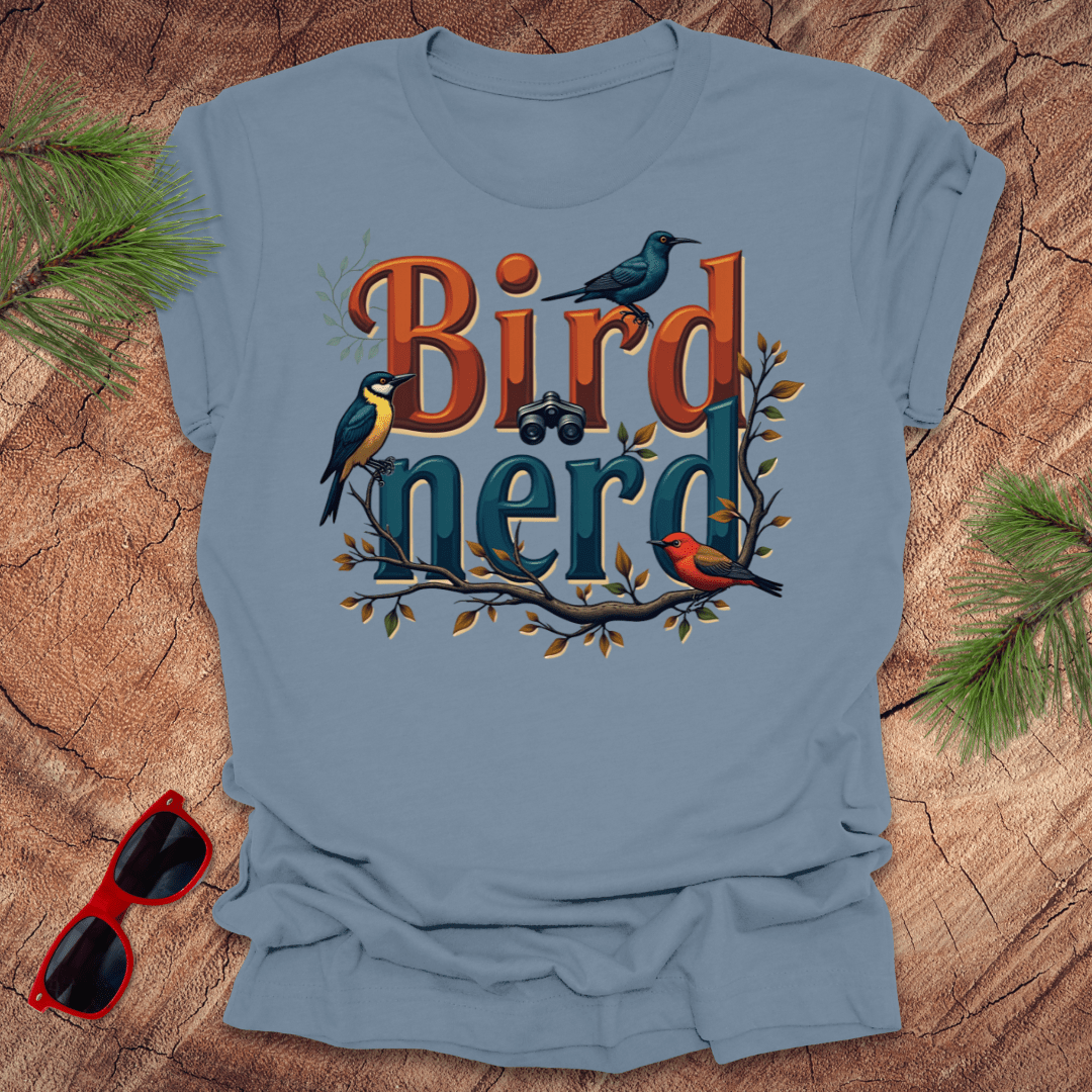 A steel blue t-shirt with a graphic print of birds and the text 'Bird nerd', surrounded by foliage and a pair of sunglasses lying next to it on a wooden surface.