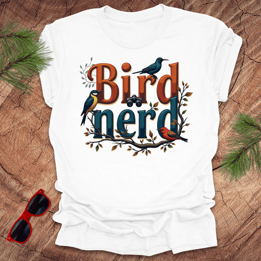 A white t-shirt with a graphic print of birds and the text 'Bird nerd', surrounded by foliage and a pair of sunglasses lying next to it on a wooden surface.