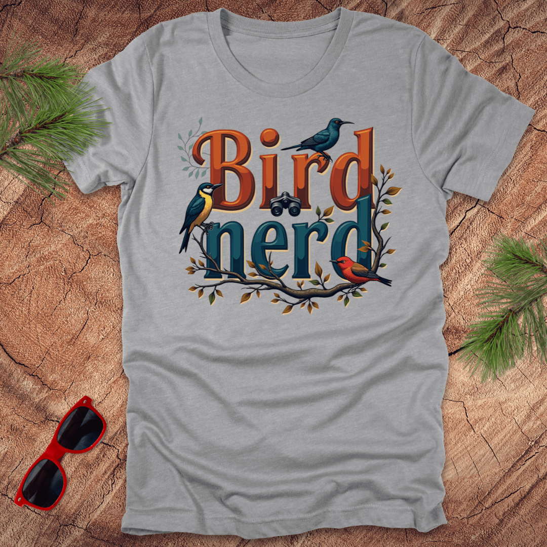 An athletic heather t-shirt with a graphic print of birds and the text 'Bird nerd', surrounded by foliage and a pair of sunglasses lying next to it on a wooden surface.
