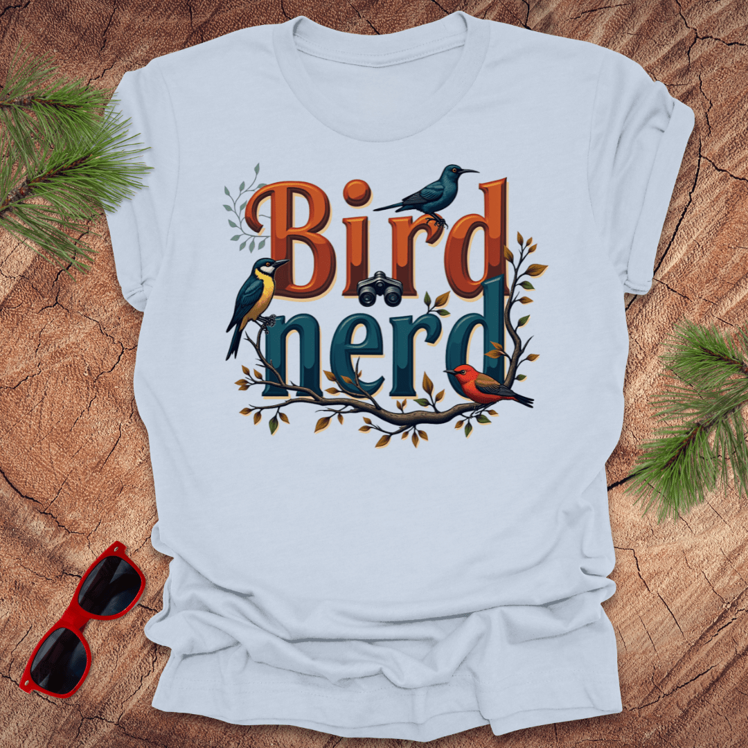 A light blue t-shirt with a graphic print of birds and the text 'Bird nerd', surrounded by foliage and a pair of binoculars lying next to it on a wooden surface.