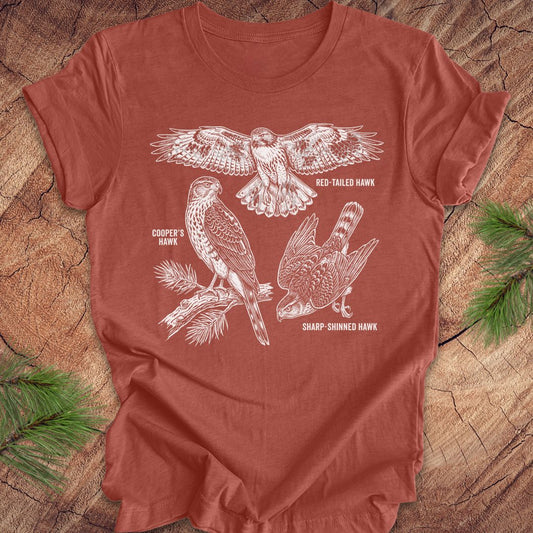 Clay colored t-shirt with hawk illustrations on a wooden surface