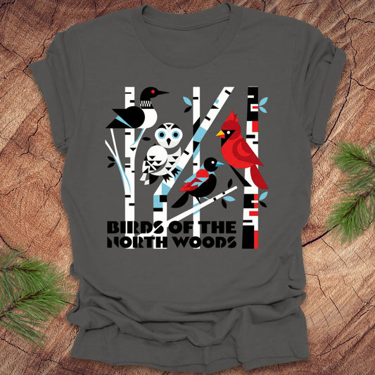 Gray t-shirt with bird design and 'Birds of the North Woods' text on a wooden surface.