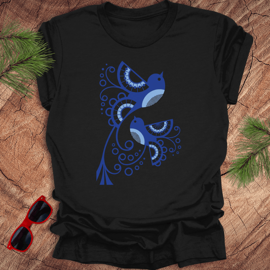 Black t-shirt with blue abstract design on a wooden surface with sunglasses and pine branches.