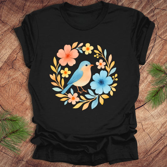 Black t-shirt with a colorful bird and floral design on a wooden surface.