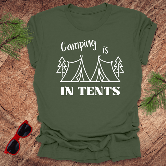 Green t-shirt with 'Camping is in tents' text and graphic on a wooden surface with sunglasses and pine branches.