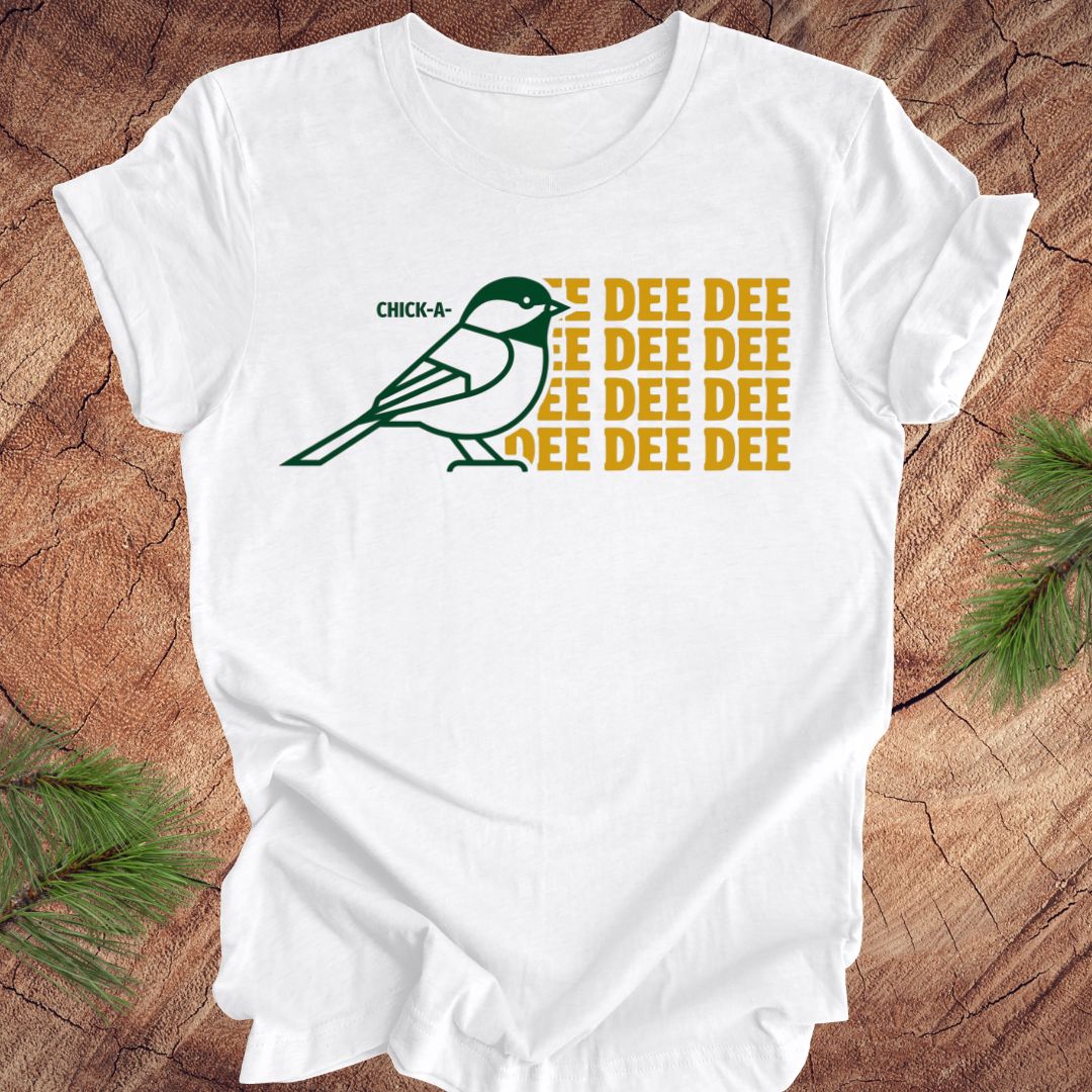 White t-shirt with a green chickadee graphic and 'DEE DEE DEE' text on a wooden surface.