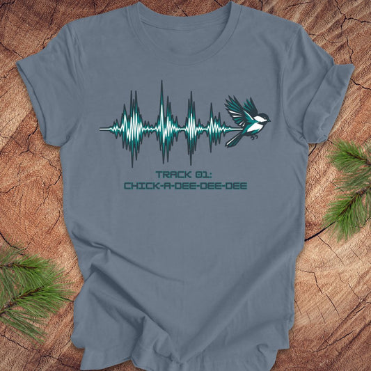 Steel blue t-shirt with a chickadee and sound wave design on a wooden surface