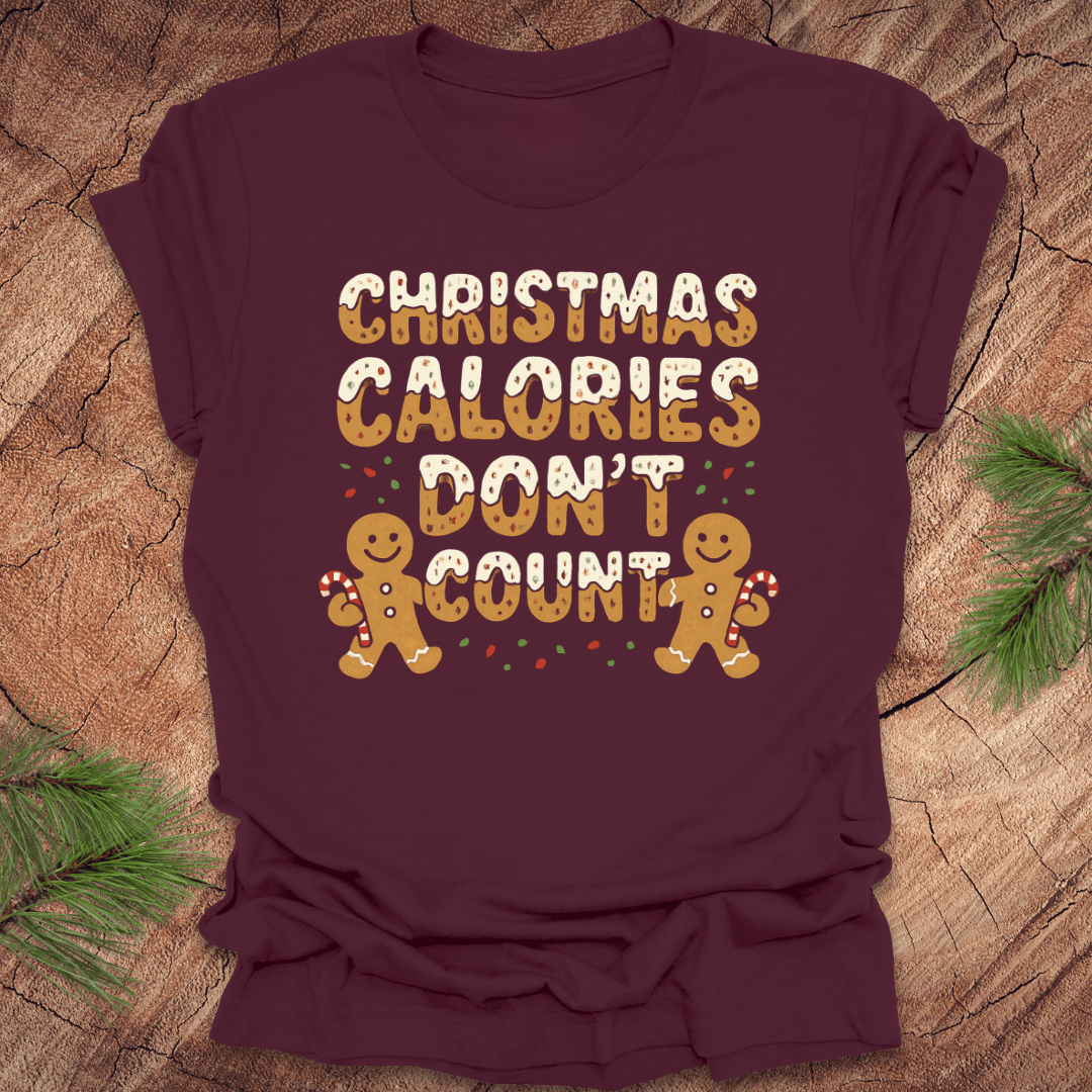 Maroon tshirt with festive gingerbread text, 'Christmas calories don't count' with gingerbread men on a wooden background.