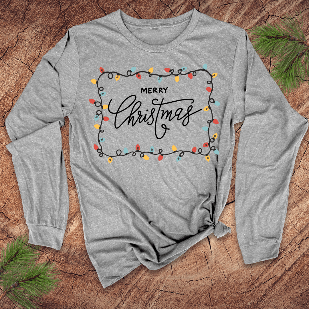 Gray long-sleeve shirt with 'Merry Christmas' design on a wooden surface with pine branches.