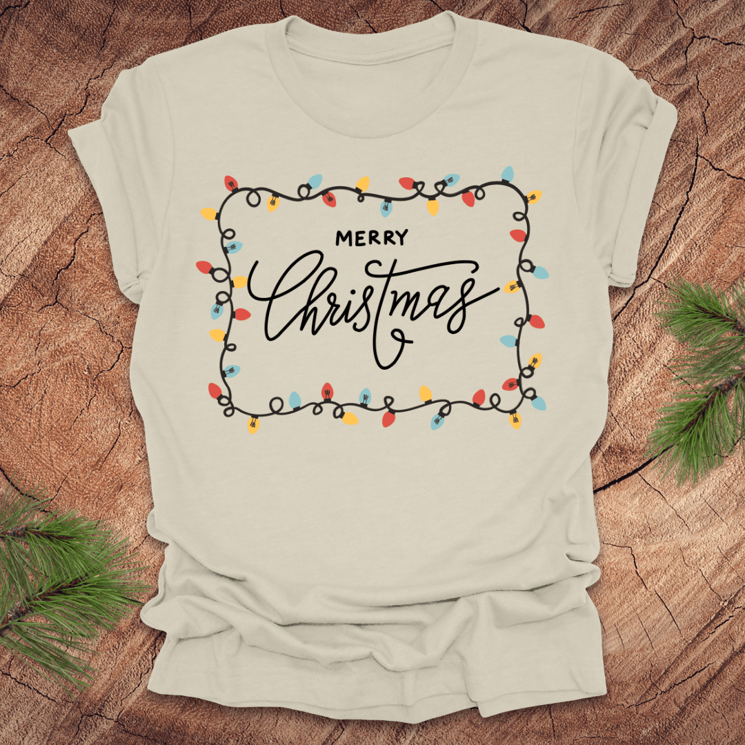 Beige t-shirt with christmas lights graphic and 'Merry Christmas' design on a wooden surface
