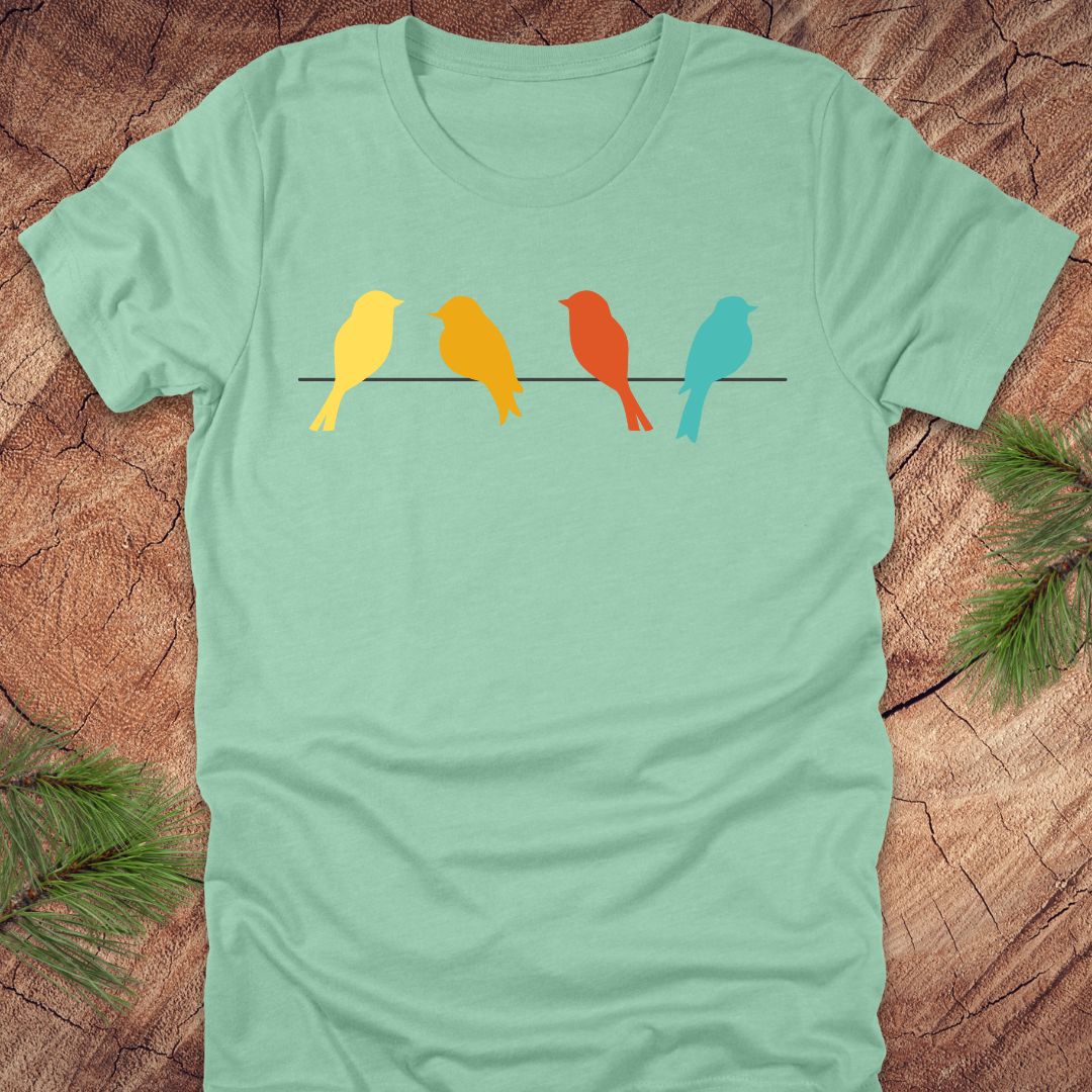 Light green t-shirt with colorful birds on a wire design on a wooden surface