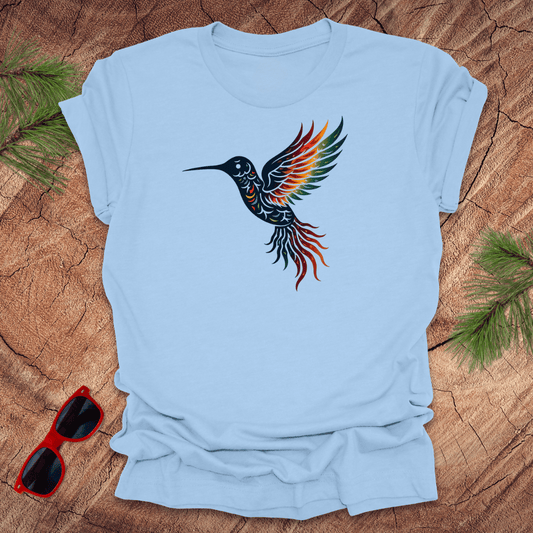 Light blue t-shirt with a colorful hummingbird design on a wooden surface with sunglasses and greenery.