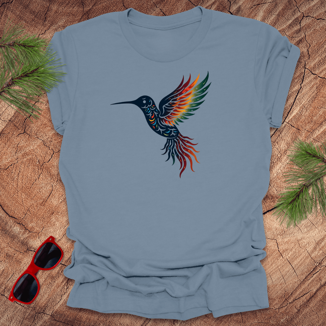 Blue t-shirt with a colorful hummingbird design on a wooden surface with sunglasses and greenery.