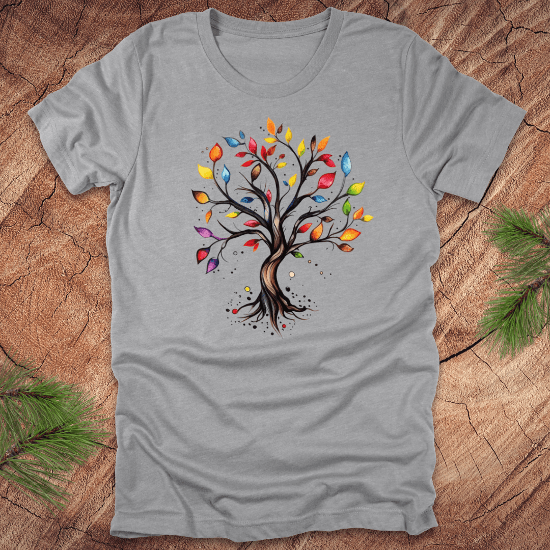 Gray tshirt with a colorful tree design on a wood background with pine leaves.