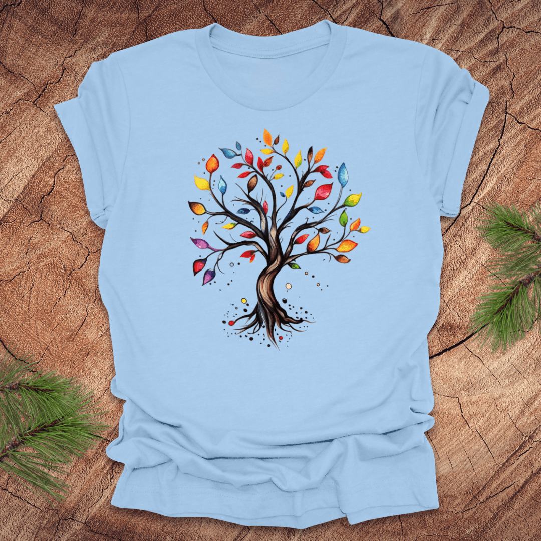Blue tshirt with a colorful tree design on a wood background with pine leaves.