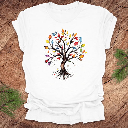 White tshirt with a colorful tree design on a wood background with pine leaves.