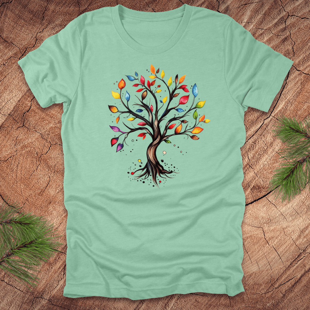 Mint green tshirt with a colorful tree design on a wood background with pine leaves.
