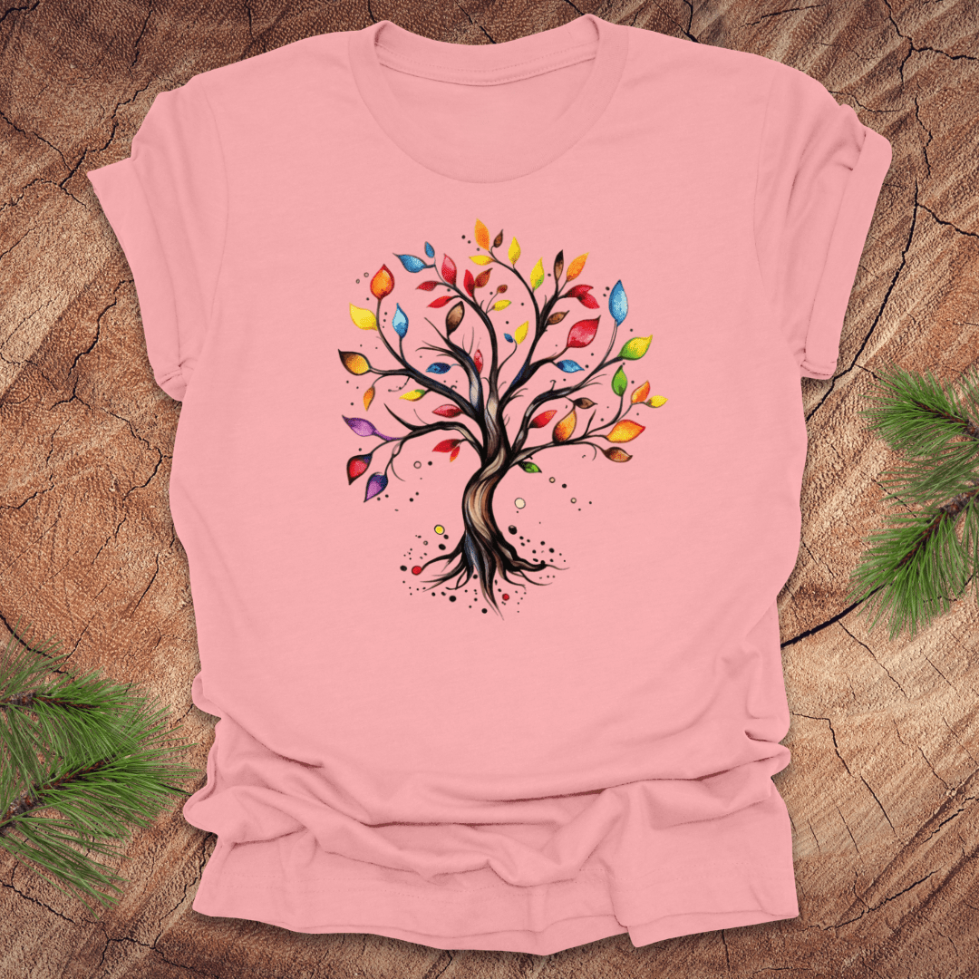 Pink tshirt with a colorful tree design on a wood background with pine leaves.