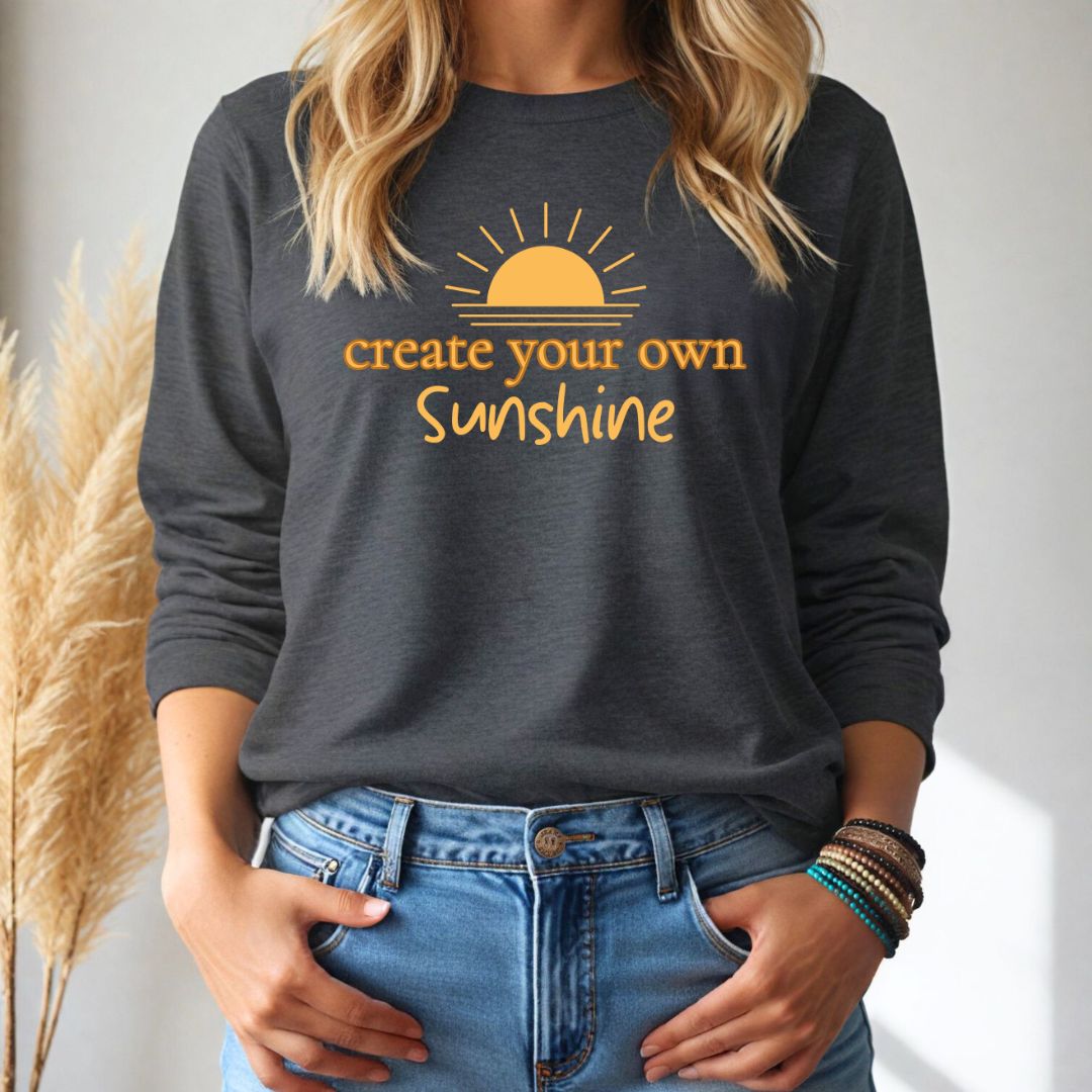 Person wearing a dark gray long-sleeve tshirt with 'create your own sunshine' text and sun graphic.