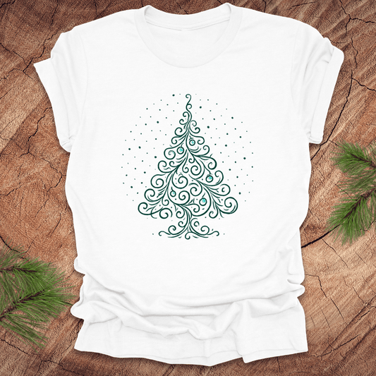 White t-shirt with a green Christmas tree design on a wooden surface with pine branches.