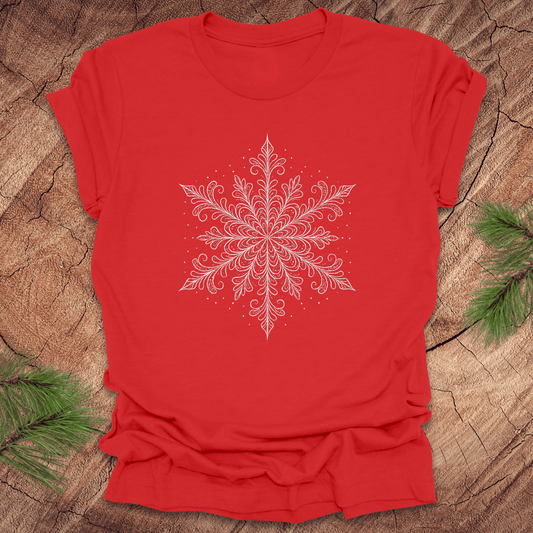 Red t-shirt with a white snowflake design on a wooden surface with greenery.