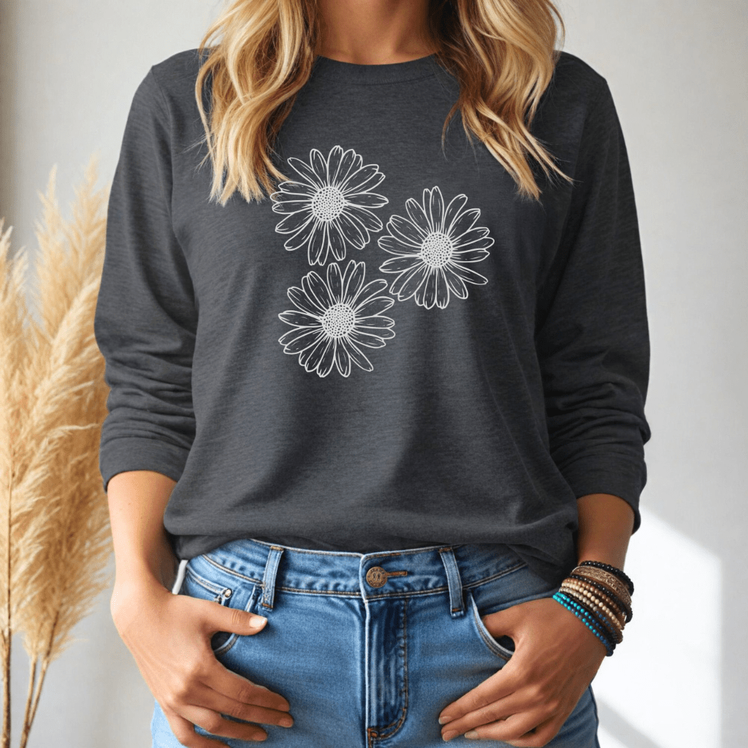 Person wearing a dark gray long sleeve tee with 3 big daisies wearing blue jeans, standing against a neutral background.
