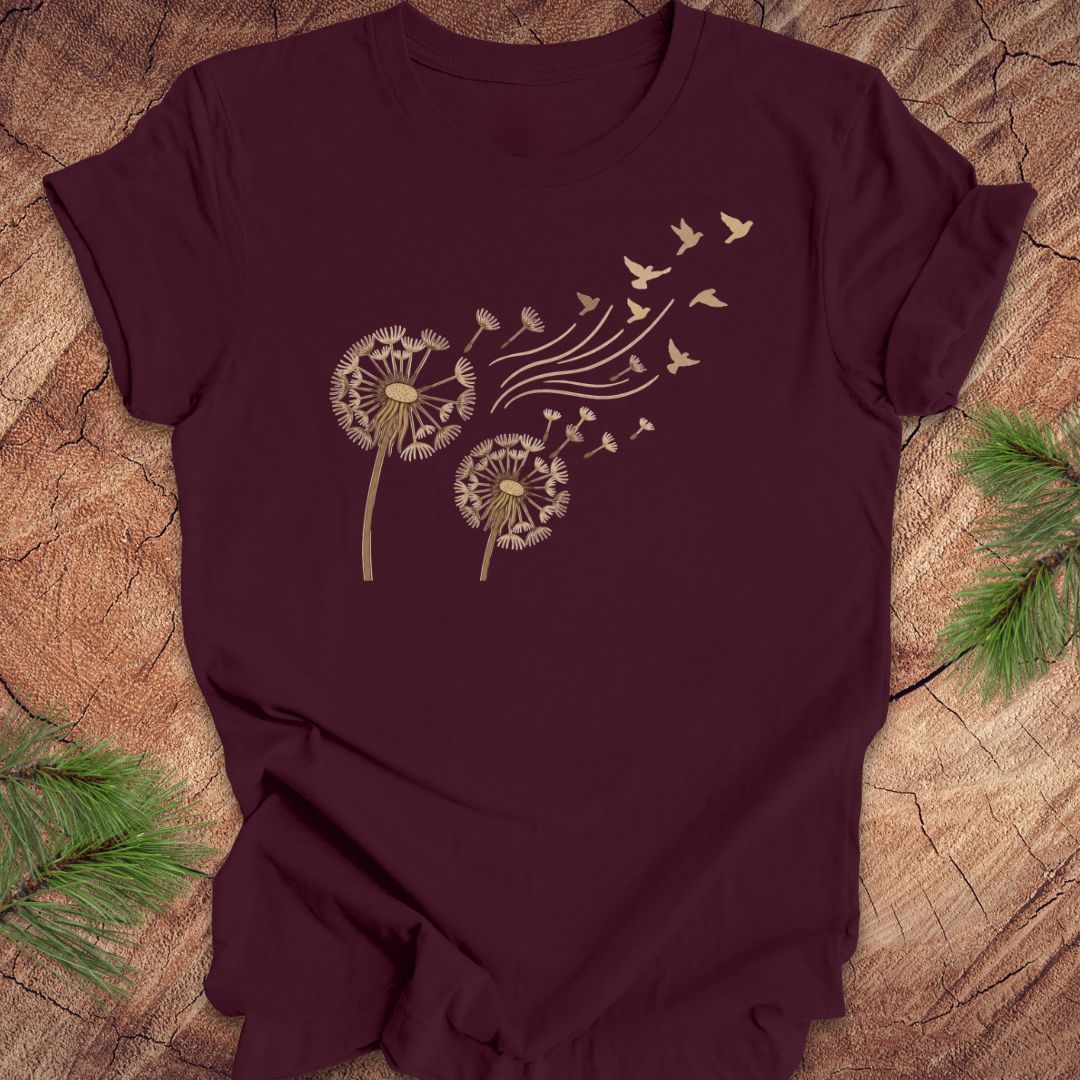 Maroon t-shirt with dandelion and bird design on a wooden surface
