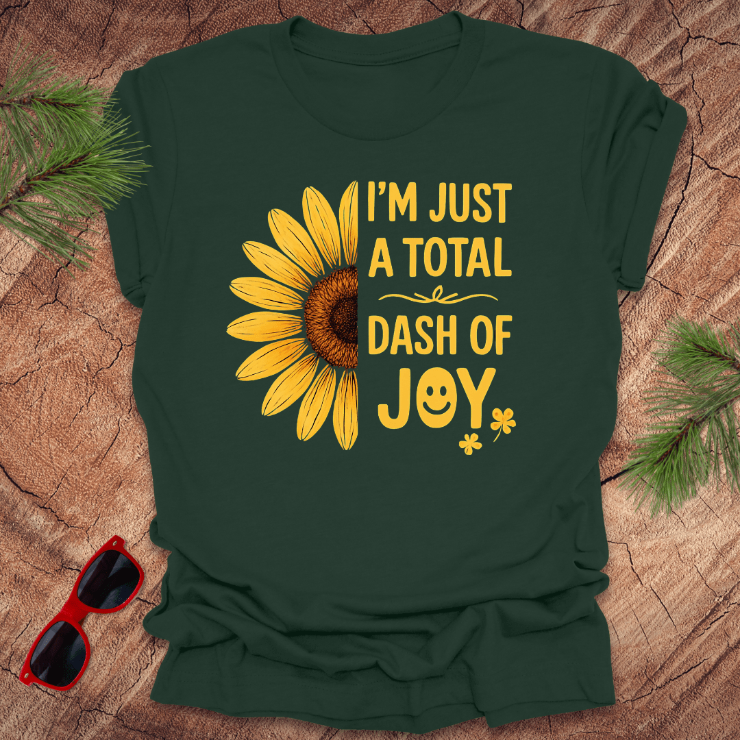 Forest Green t-shirt with sunflower graphic and text 'i'm just a total dash of joy' on a wooden surface with sunglasses and pine branches.