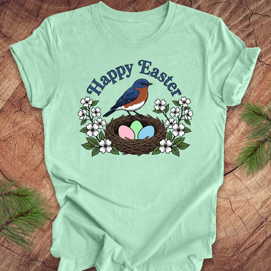 Light green t-shirt with 'Happy Easter' design featuring a bluebird, nest, and eggs on a wooden surface.