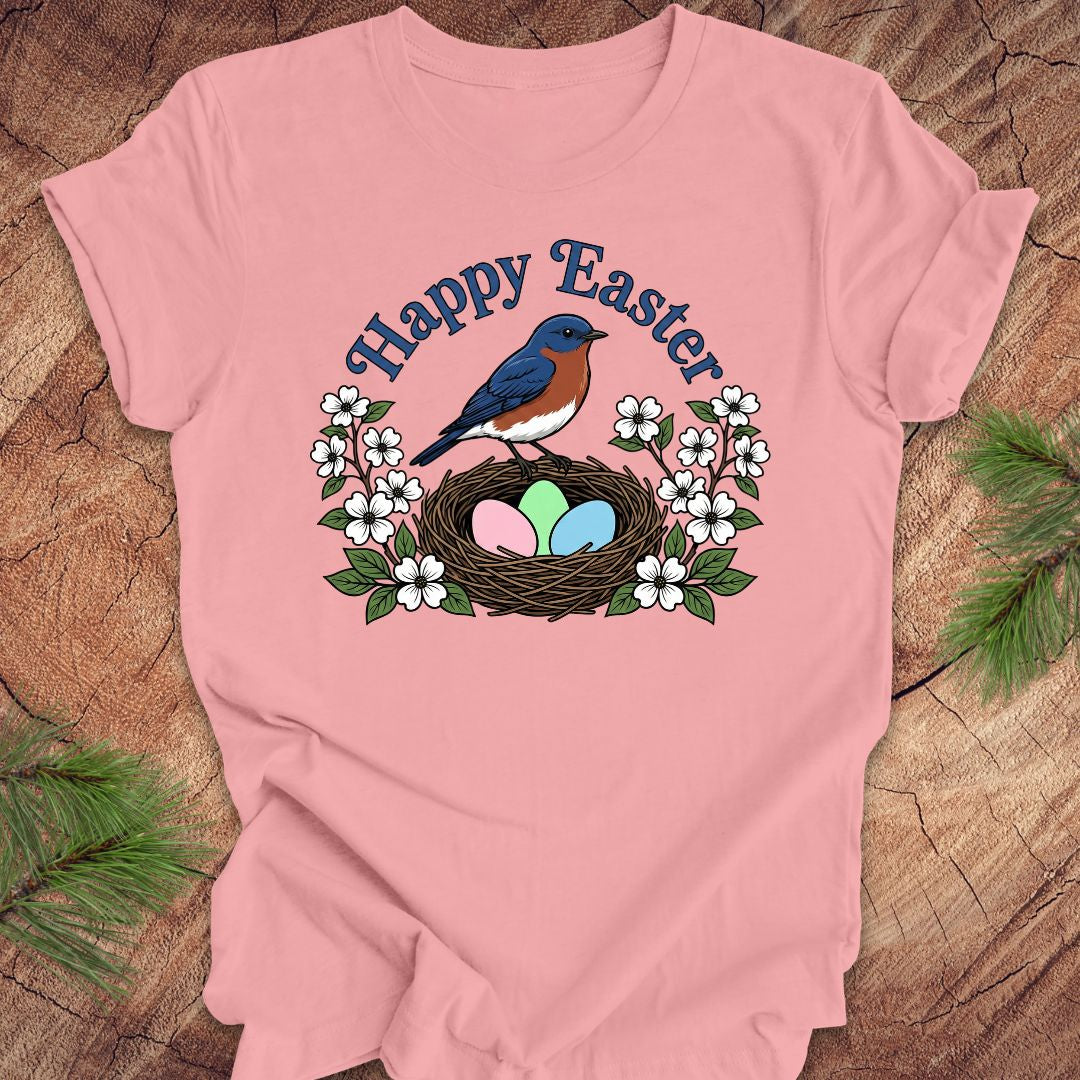 Pink t-shirt with Easter design featuring a bluebird, nest, and eggs on a wooden background.