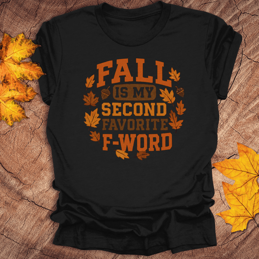 Black t-shirt with orange text 'FALL IS MY SECOND FAVORITE F-WORD' on a wooden surface with autumn leaves.