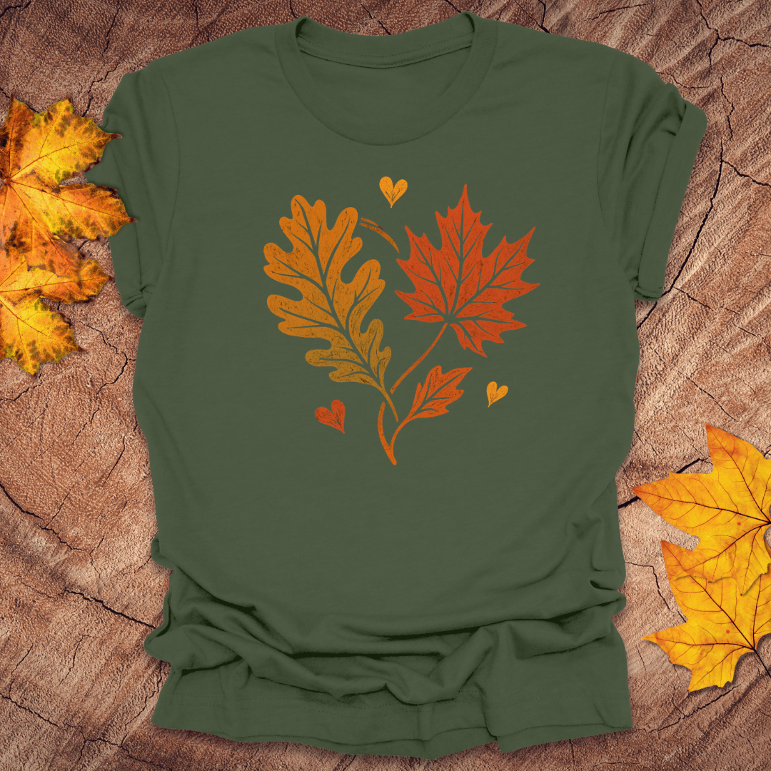 Green t-shirt with autumn leaf design in the shape of a heart on a textured surface with fall leaves.