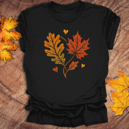 Black t-shirt with autumn leaf design in the shape of a heart on a textured surface with fall leaves.