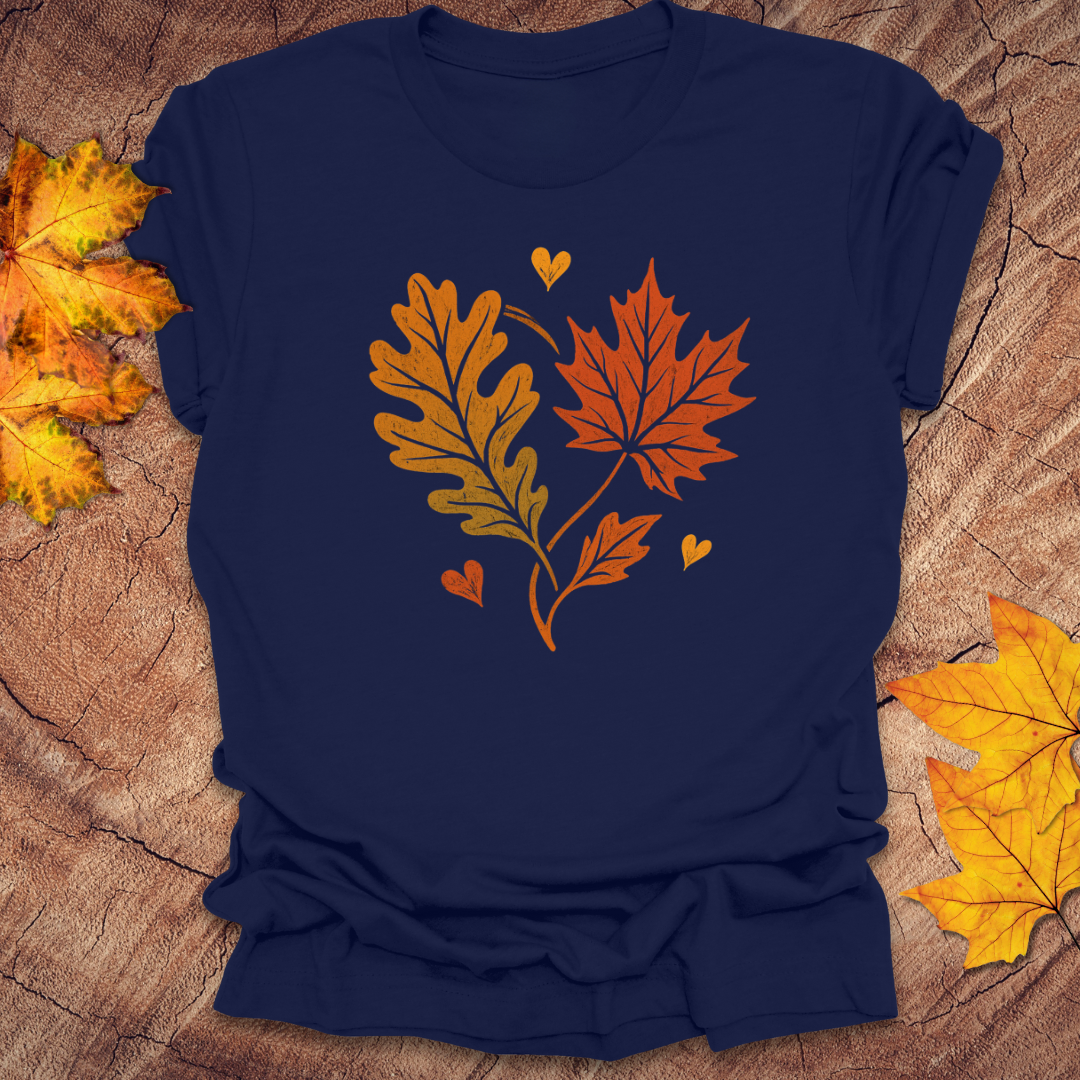 Navy t-shirt with autumn leaf design in the shape of a heart on a textured surface with fall leaves.