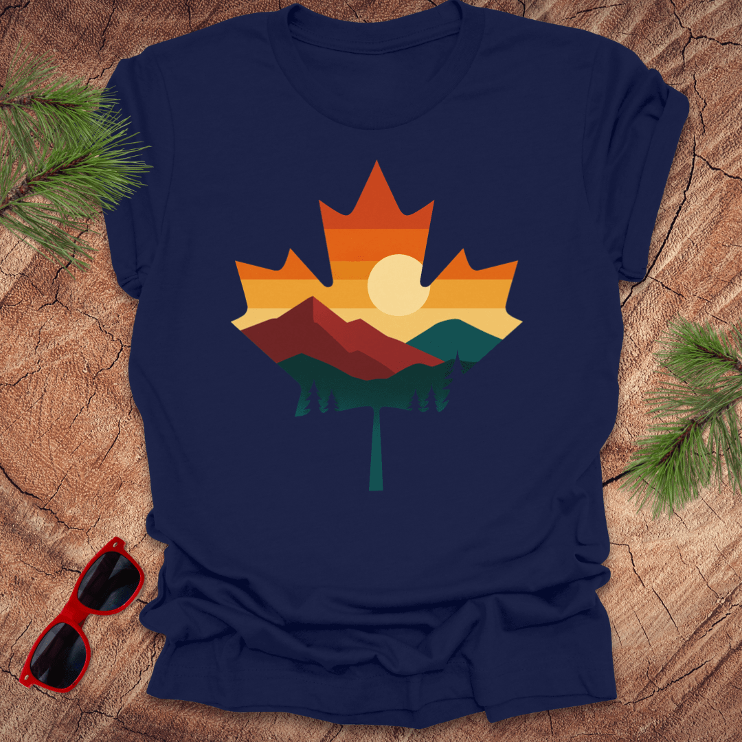 Navy blue t-shirt with a colorful maple leaf design on a wooden surface with sunglasses and pine branches.