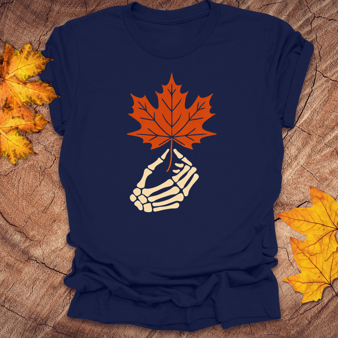 Navy blue t-shirt with a skeleton hand holding an orange maple leaf on a wooden surface with fall leaves.