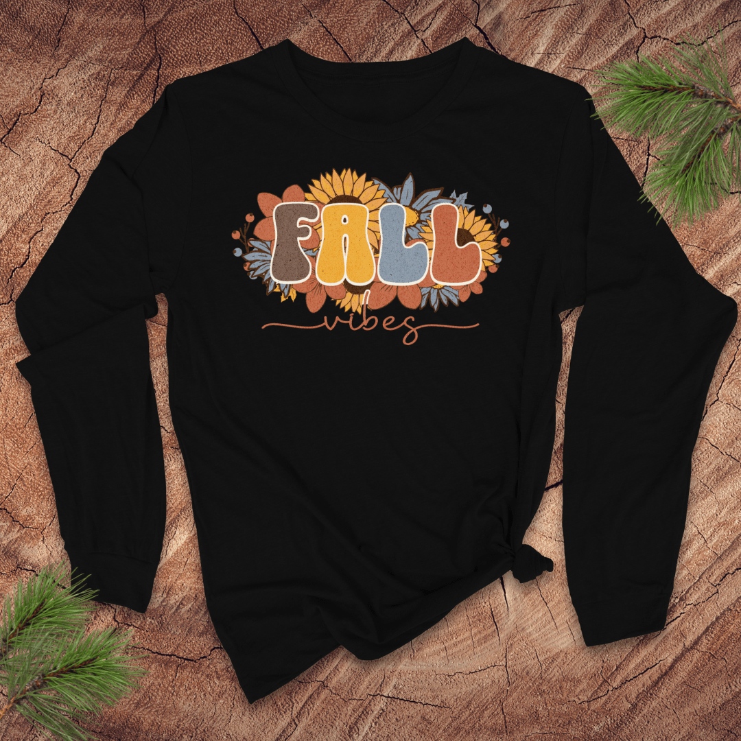 Black long sleeve tshirt with 'Fall Vibes' text on a wooden surface with pine branches.