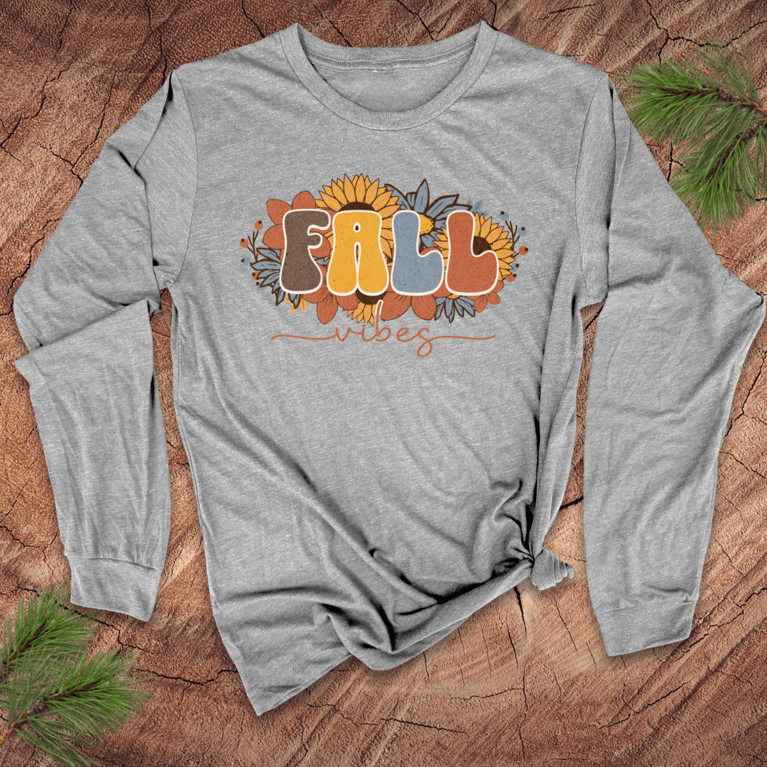 Gray long-sleeve shirt with 'FALL VIBES' text and sunflower design on a wooden surface